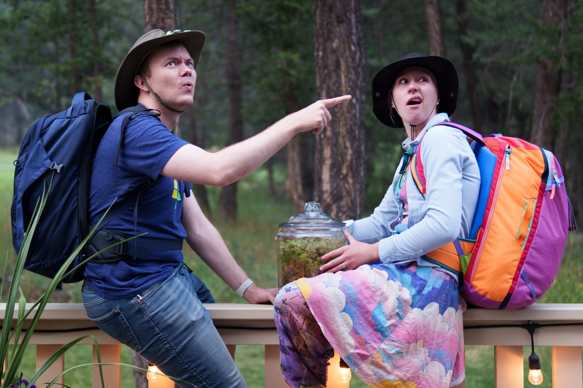 Rachel and Johann sitting on a railing, wearing backpacking gear, looking really really confused.