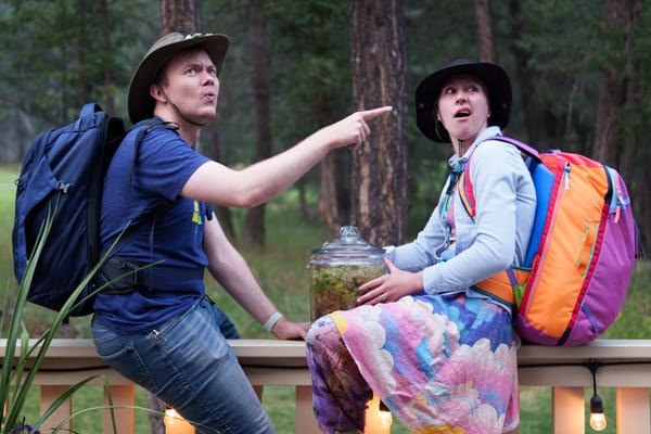 Rachel and Johann sitting on a railing, wearing backpacking gear, looking really really confused.